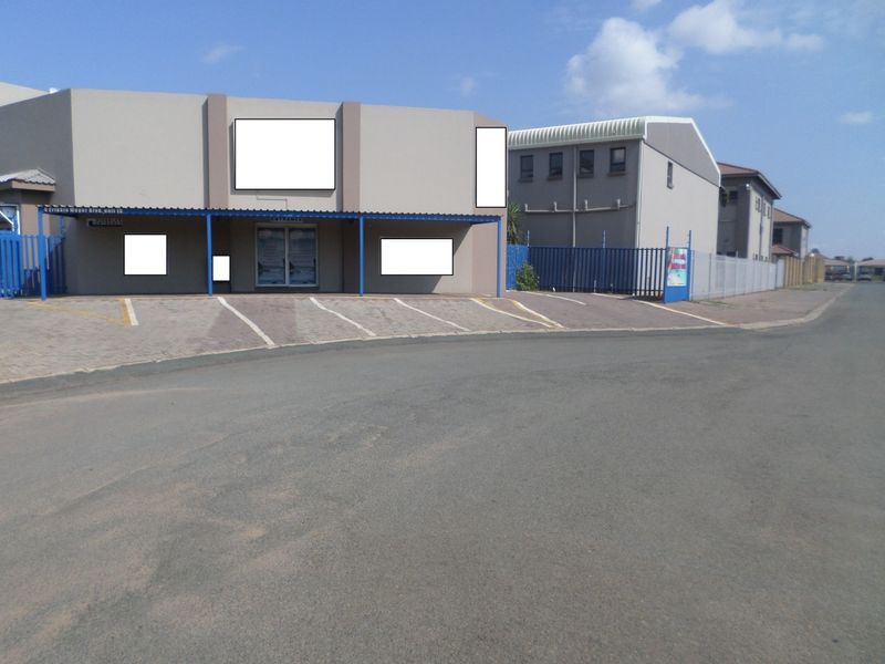 Front exterior view of a commercial property featuring a paved parking area, covered entrance walkway, and secure perimeter fencing.