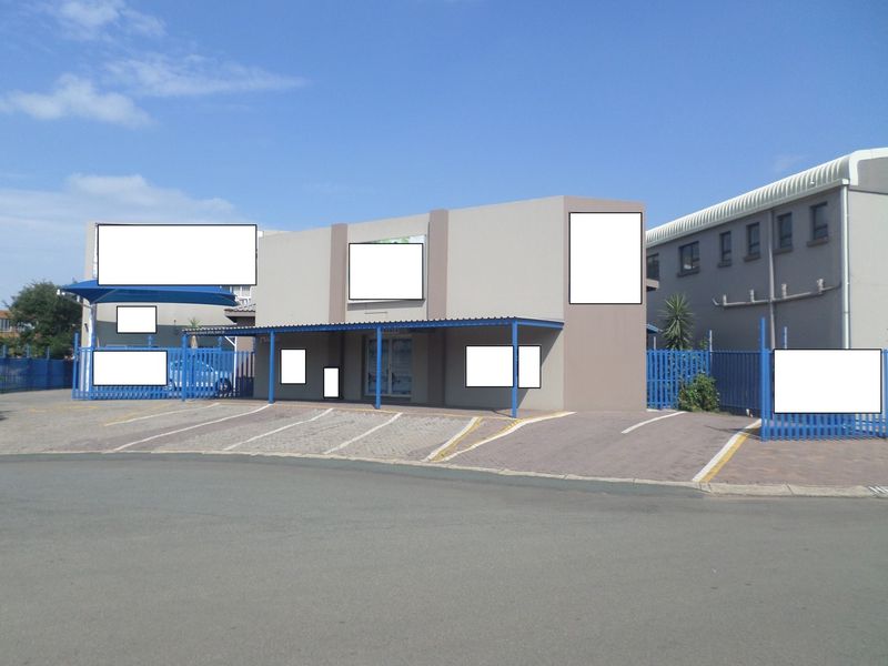 Front exterior view of a commercial property featuring a paved parking area, covered parking bays, and secure metal perimeter fencing.
