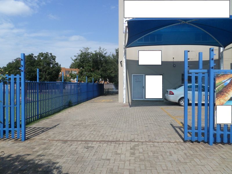 Commercial property entrance featuring a paved driveway, secure steel fencing, electric security measures, and a shaded parking area.