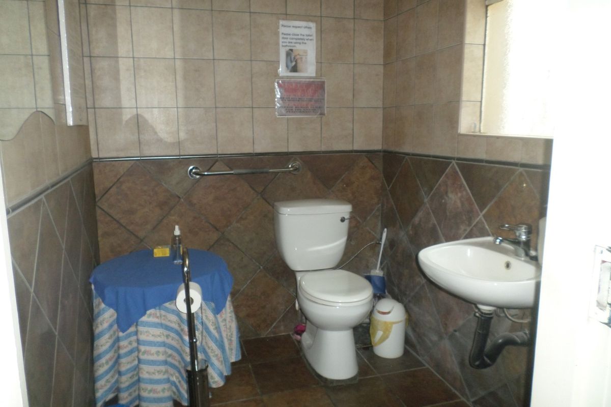 A functional commercial bathroom featuring tiled walls and floors, a standard toilet, and a pedestal washbasin with a chrome faucet.