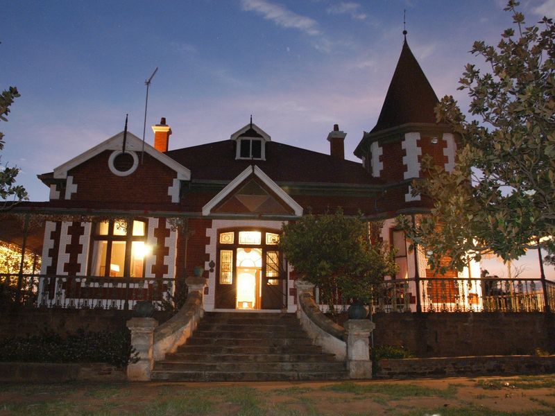 A charming historic brick guest house featuring a prominent turret, stone staircase entrance, and classic architectural detailing captured at twilight.
