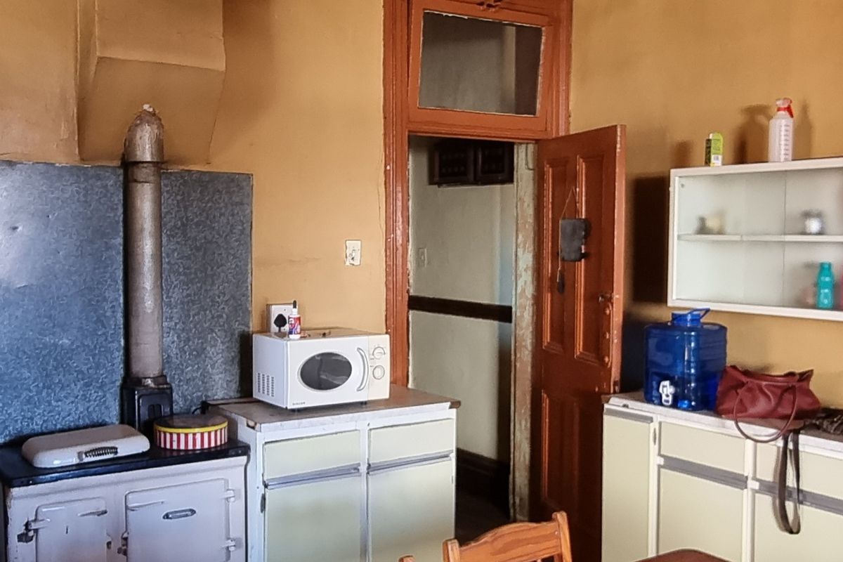 A dated kitchen featuring a combination of gas and solid fuel stoves, built-in cabinetry, and wall-mounted shelving with original timber door frames.
