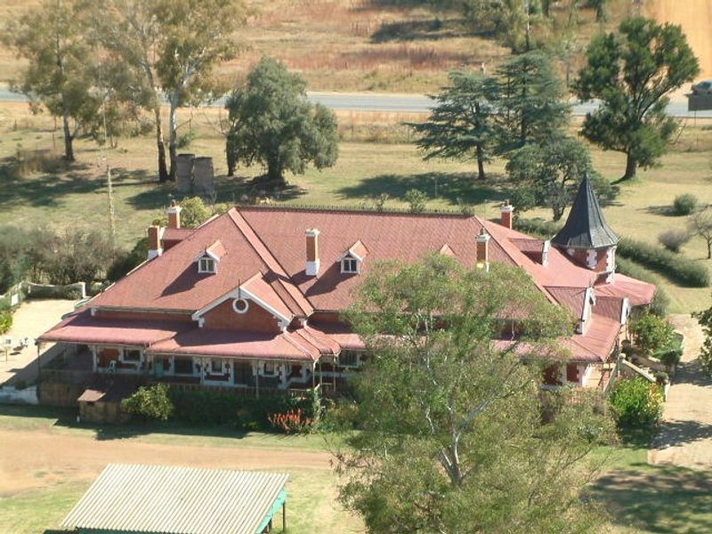 Aerial view of a large guest house featuring a distinctive red tiled roof, multiple chimneys, dormer windows, and a turret.