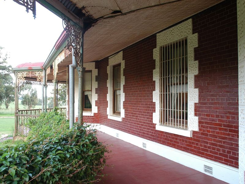 A covered veranda featuring classic brickwork, decorative wrought iron lacework, and a pressed metal ceiling, offering a traditional architectural aesthetic.