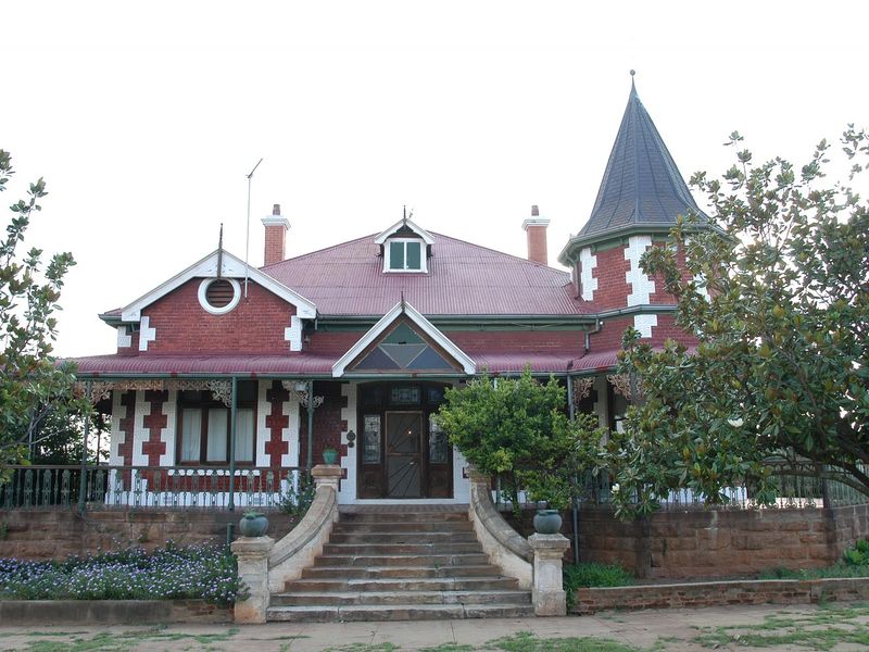 A charming historic guest house featuring classic red brick architecture, a prominent turret, a covered veranda, and an elegant stone staircase entrance.