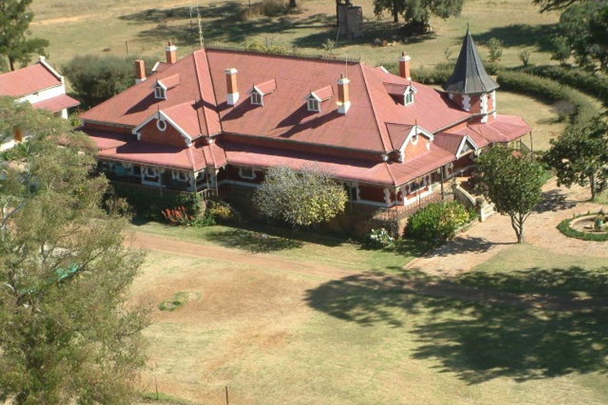 An elevated aerial view of a large, historic-style guest house featuring a prominent red pitched roof, multiple chimneys, and a distinctive turret.
