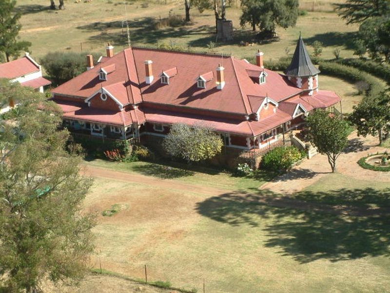 An elevated aerial view of a large, historic-style guest house featuring a prominent red pitched roof, multiple chimneys, and a distinctive turret.