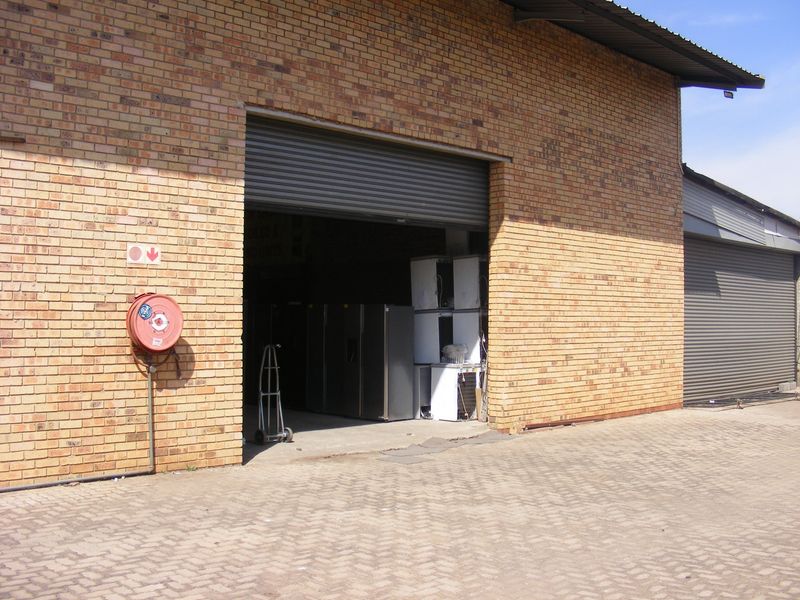 Industrial warehouse unit featuring a face brick exterior, large roller shutter door access, and a dedicated fire hose reel installation.