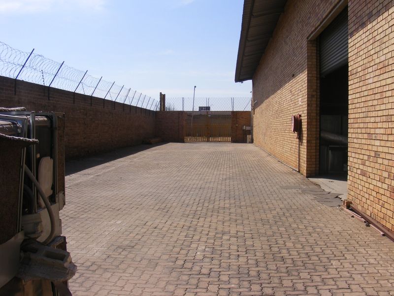 Secure industrial rear yard featuring paved flooring, high brick perimeter walls with razor wire, and a large roller shutter access point.