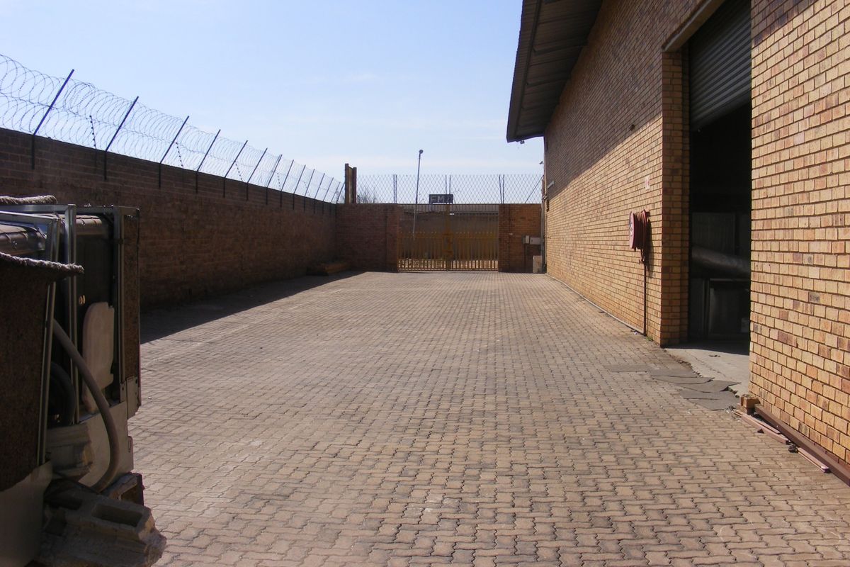 Secure industrial rear yard featuring paved flooring, high brick perimeter walls with razor wire, and a large roller shutter access point.