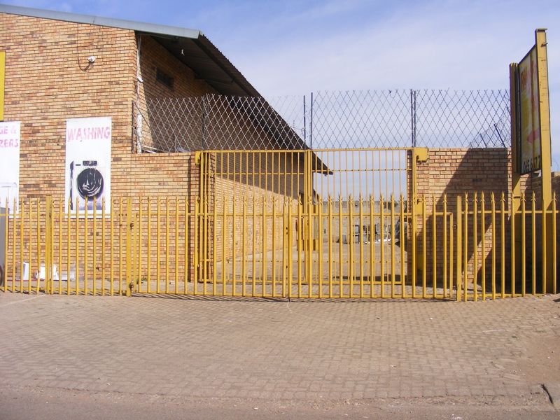 Industrial property frontage featuring a secure gated entrance, brick facade, and perimeter security fencing with razor wire.