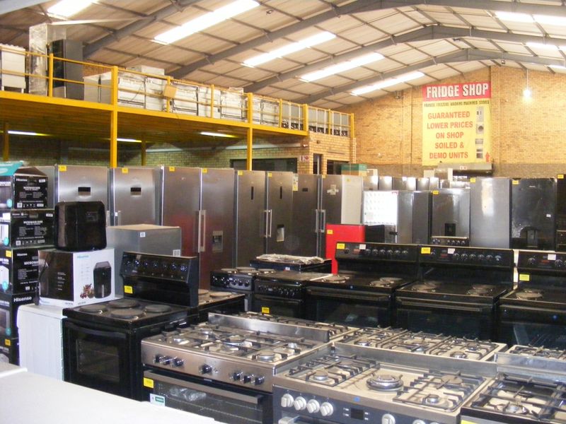 Industrial warehouse space featuring a mezzanine level, exposed steel roof trusses, and brickwork walls, currently utilized for appliance retail.