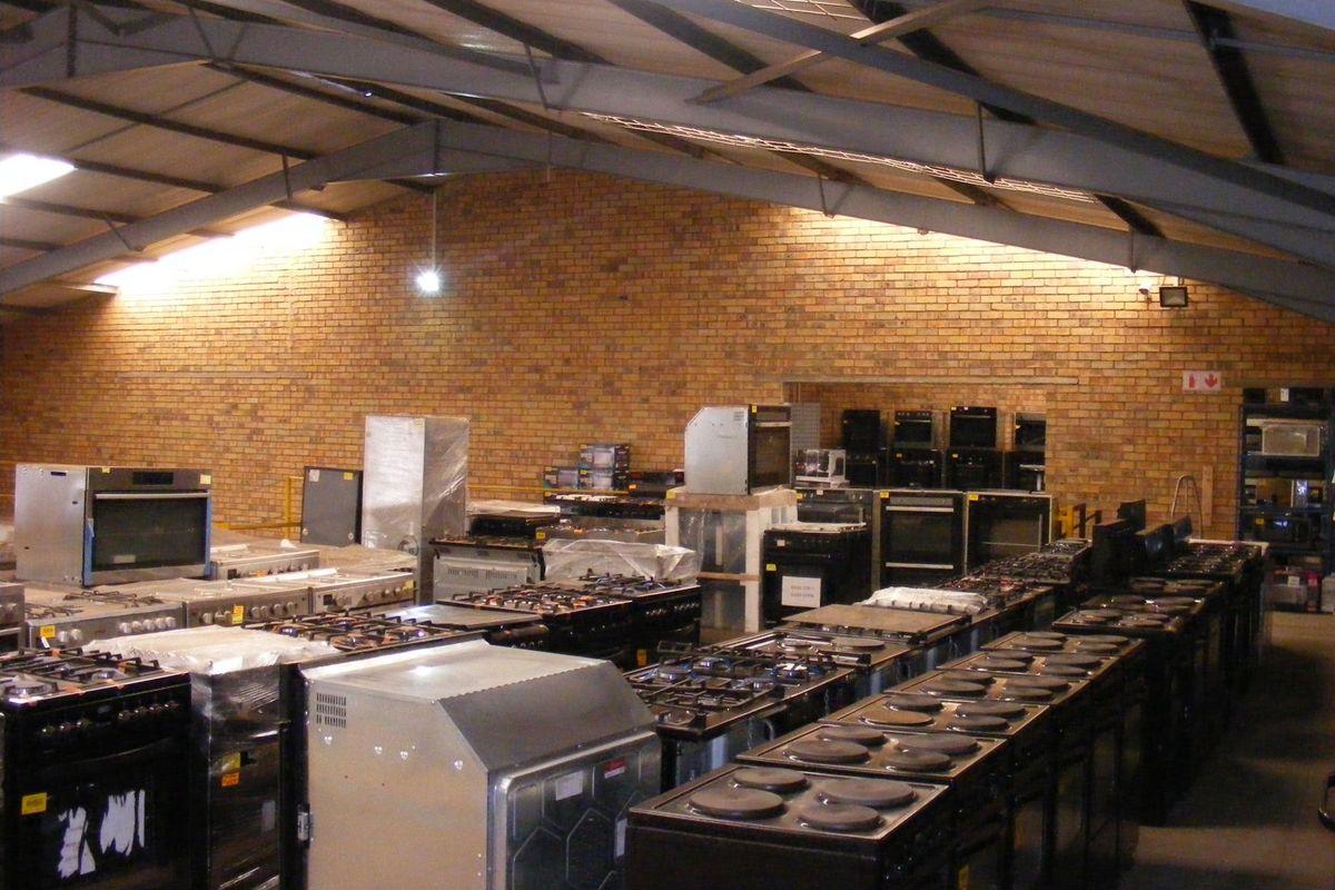 Large industrial warehouse space featuring exposed brick walls and steel roof trusses, currently utilized for appliance storage.