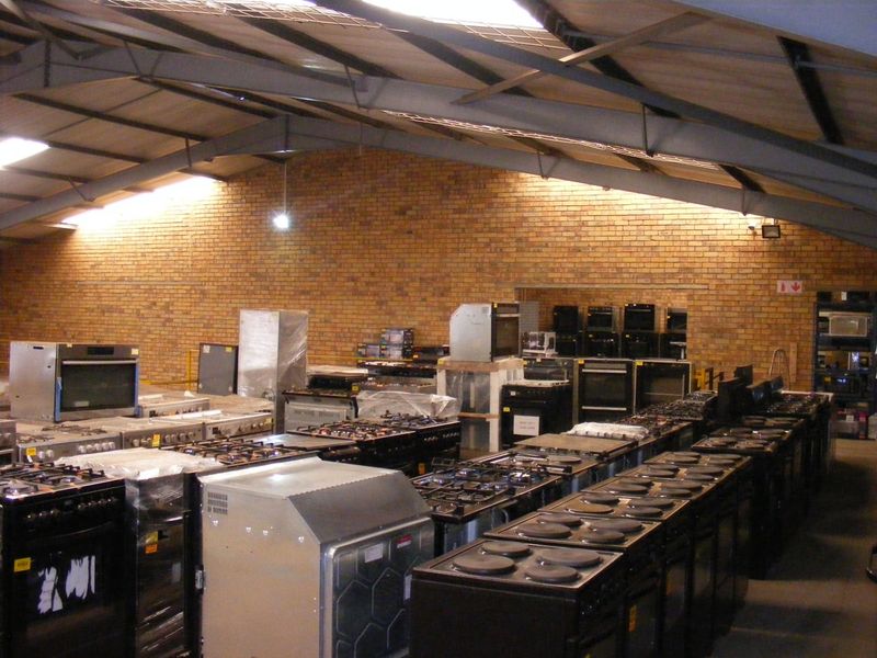Large industrial warehouse space featuring exposed brick walls and steel roof trusses, currently utilized for appliance storage.