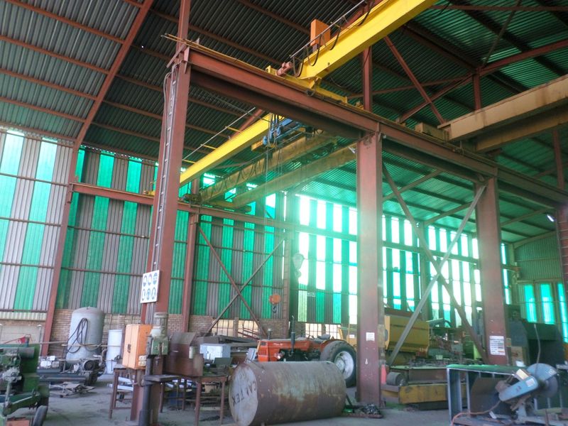 Industrial warehouse space featuring a high-clearance overhead gantry crane, steel portal frame construction, and translucent wall panels providing natural light.