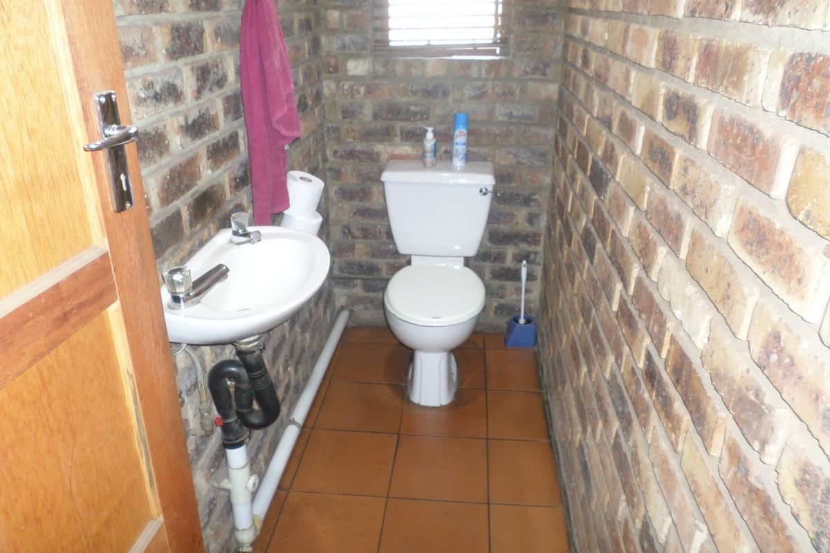 A compact industrial-style bathroom featuring exposed brick walls, ceramic floor tiles, a wall-mounted basin, and a standard toilet.