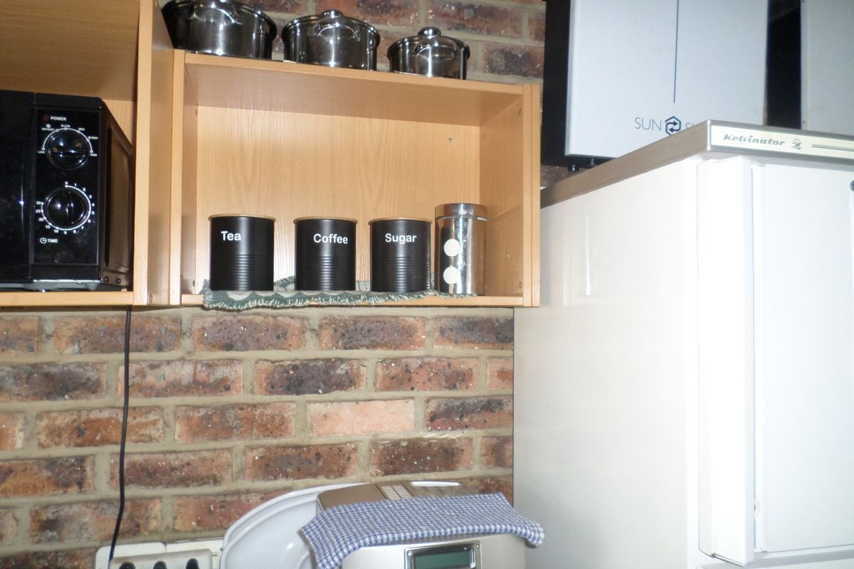 A kitchen area featuring exposed brick walls, laminate cabinetry, and a wall-mounted inverter system.