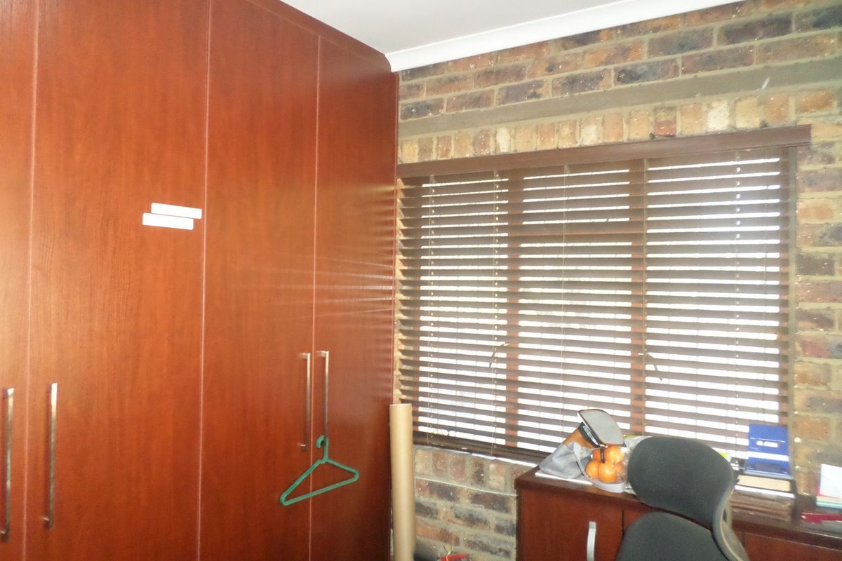 Bedroom featuring floor-to-ceiling built-in wooden cupboards and an exposed brick wall with fitted venetian blinds.