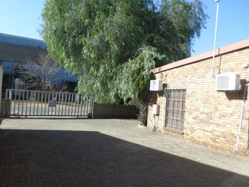 Rear exterior view of the industrial property featuring a paved yard, brick facade, security gate, and mounted air conditioning units.