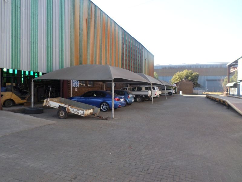 Industrial property exterior featuring a large warehouse with corrugated metal cladding and a covered parking area with shade cloth structures.