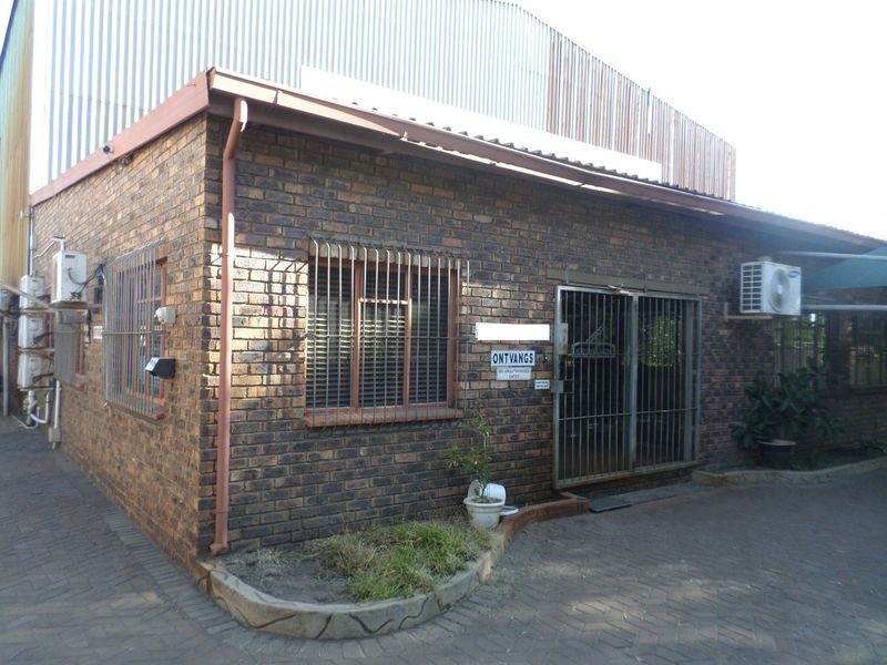 Industrial building exterior featuring face brick construction, security bars on windows, and multiple wall-mounted air conditioning units with a paved entrance area.