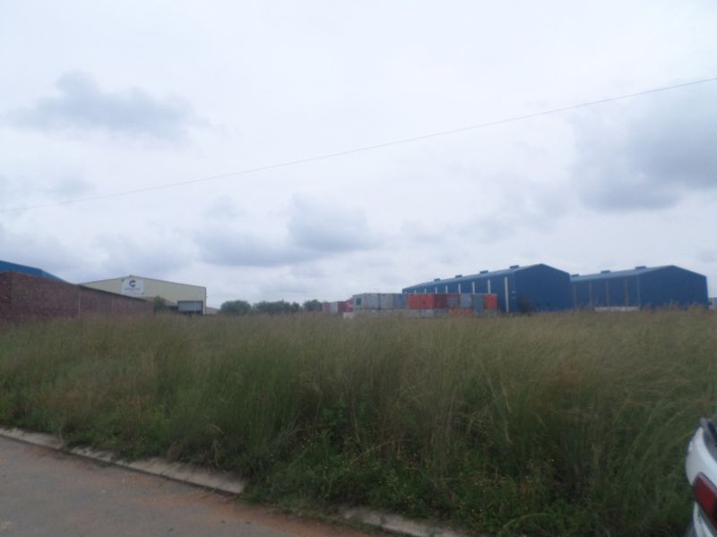 View of industrial warehouse buildings and surrounding vacant land with overgrown grass and perimeter walling.