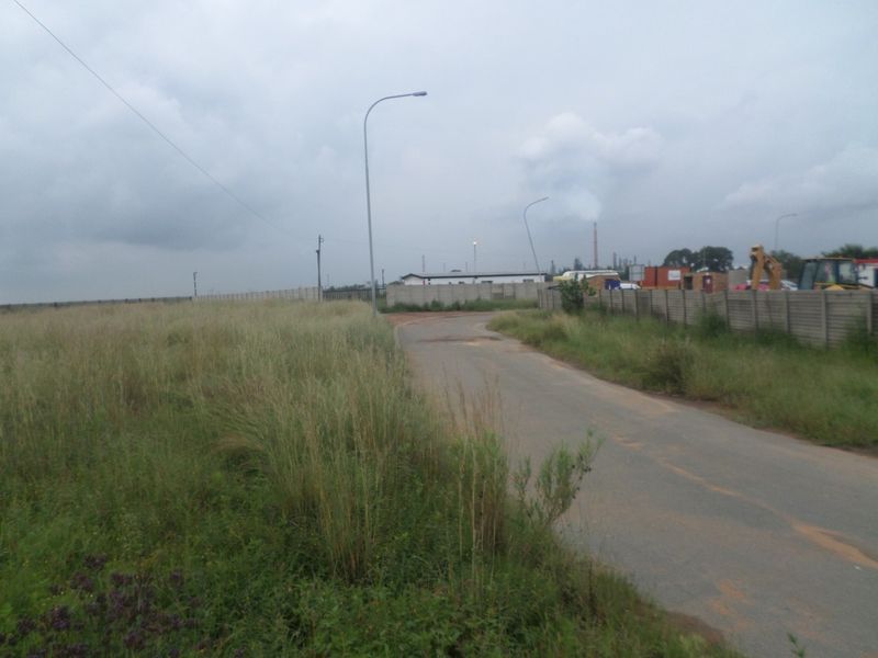 A view of an industrial access road featuring asphalt paving, street lighting, and precast concrete perimeter fencing.