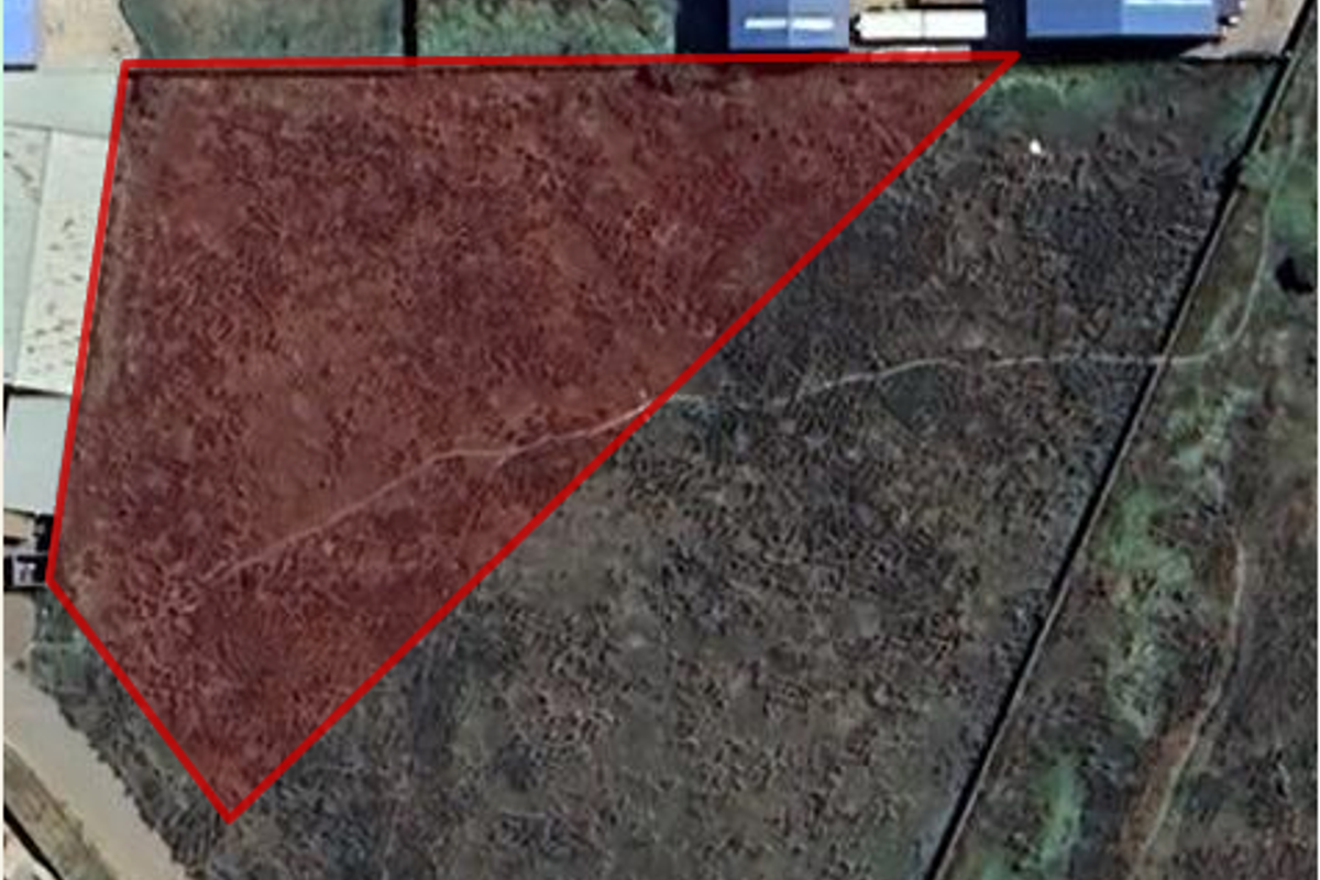 Aerial view of an industrial land parcel with a highlighted boundary, showing undeveloped terrain adjacent to existing industrial structures.