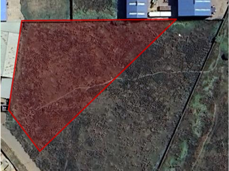 Aerial view of an industrial land parcel with a highlighted boundary, showing undeveloped terrain adjacent to existing industrial structures.