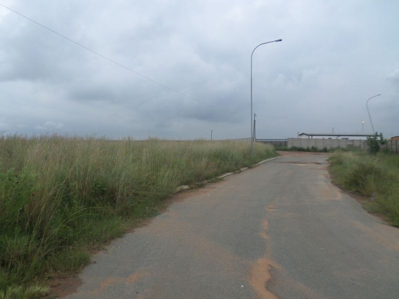 View of an industrial access road featuring asphalt paving, street lighting, and perimeter boundary walling.