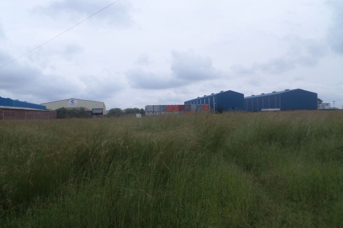 View of industrial warehouse buildings and shipping containers situated on a large plot with overgrown grass.