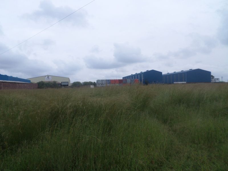 View of industrial warehouse buildings and shipping containers situated on a large plot with overgrown grass.