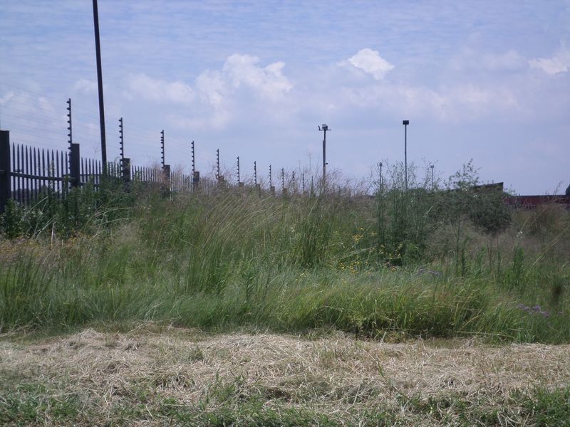 A view of a vacant commercial plot featuring perimeter security fencing with electric wires and installed security lighting poles.