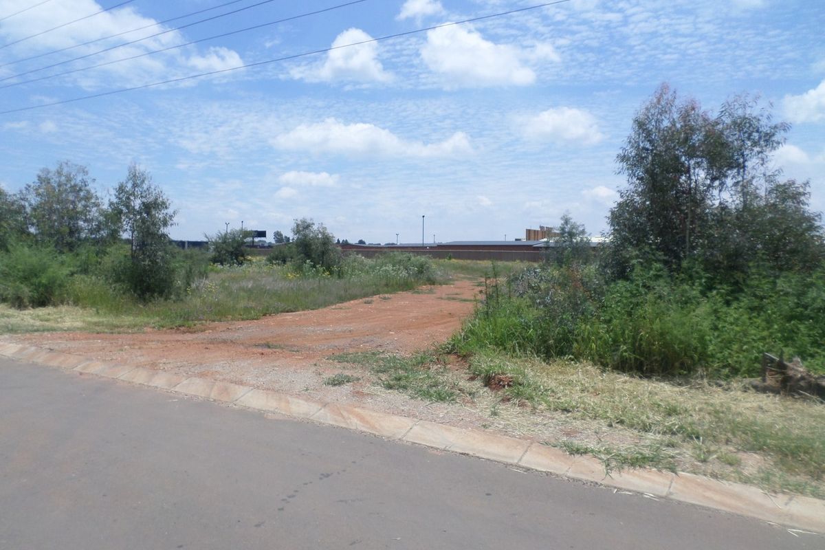 A street-level view of a vacant commercial plot featuring an unpaved access point from the adjacent asphalt road.