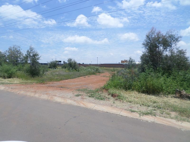 A street-level view of a vacant commercial plot featuring an unpaved access point from the adjacent asphalt road.