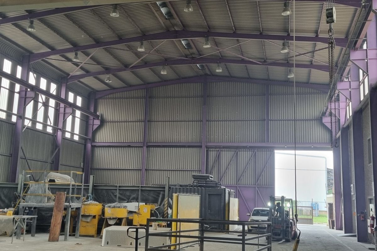 Spacious industrial warehouse featuring a high-clearance steel portal frame, corrugated metal walls, overhead crane system, and high-bay lighting with large roller door access.