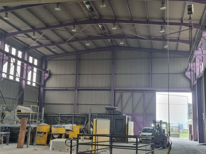 Spacious industrial warehouse featuring a high-clearance steel portal frame, corrugated metal walls, overhead crane system, and high-bay lighting with large roller door access.