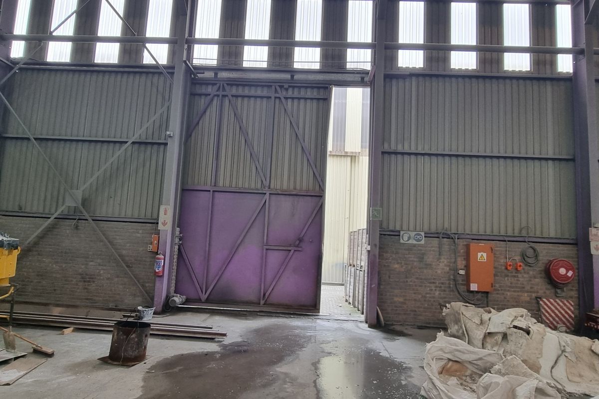 Spacious industrial utility area featuring high ceilings with translucent panels, large sliding access door, and durable concrete flooring suitable for warehouse or manufacturing operations.