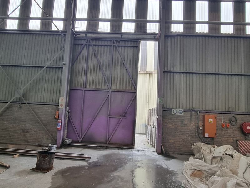Spacious industrial utility area featuring high ceilings with translucent panels, large sliding access door, and durable concrete flooring suitable for warehouse or manufacturing operations.