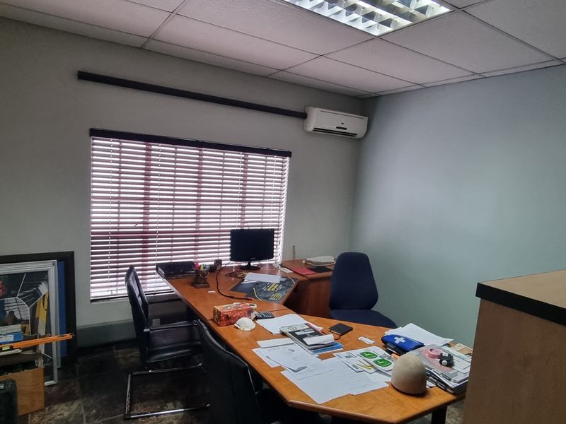 A functional office space featuring a suspended ceiling with recessed lighting, a wall-mounted air conditioning unit, and window blinds.