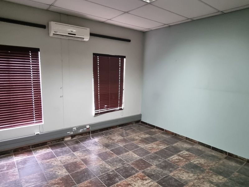 An empty office space featuring tiled flooring, a suspended ceiling, split-system air conditioning, and window blinds, suitable for a professional workspace.