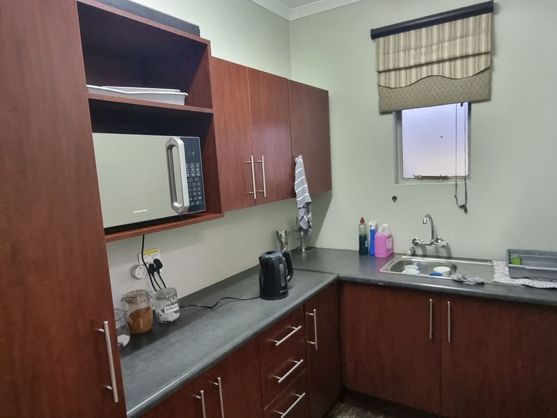 A functional scullery area featuring dark wood-finish cabinetry, laminate countertops, a stainless steel sink, and a built-in microwave unit.