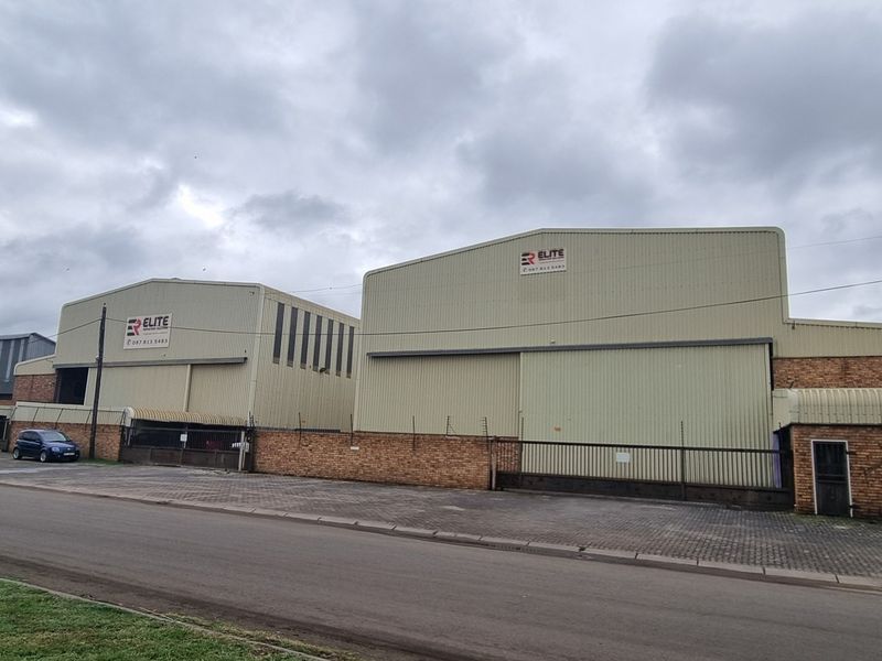 Industrial property featuring two large warehouse units with corrugated metal cladding, secure perimeter brick walls, and gated access from the street.