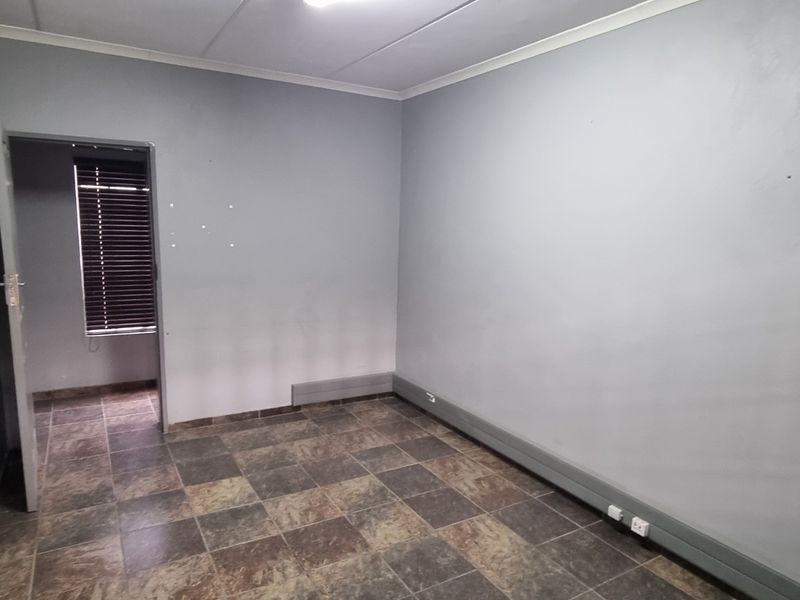 An empty office space featuring tiled flooring, grey painted walls, surface-mounted electrical trunking, and a window fitted with venetian blinds.