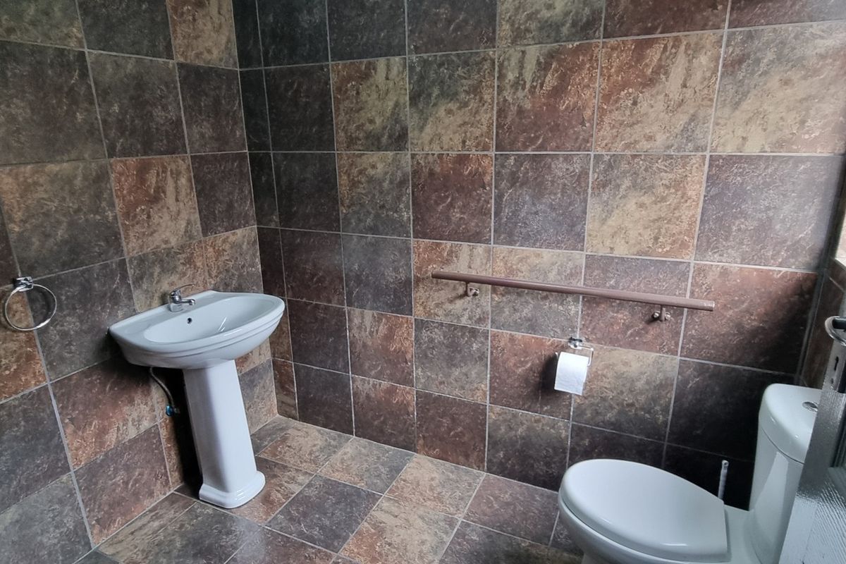 A functional bathroom featuring full-height wall tiling, a pedestal washbasin, a toilet, and a wall-mounted grab rail for accessibility.