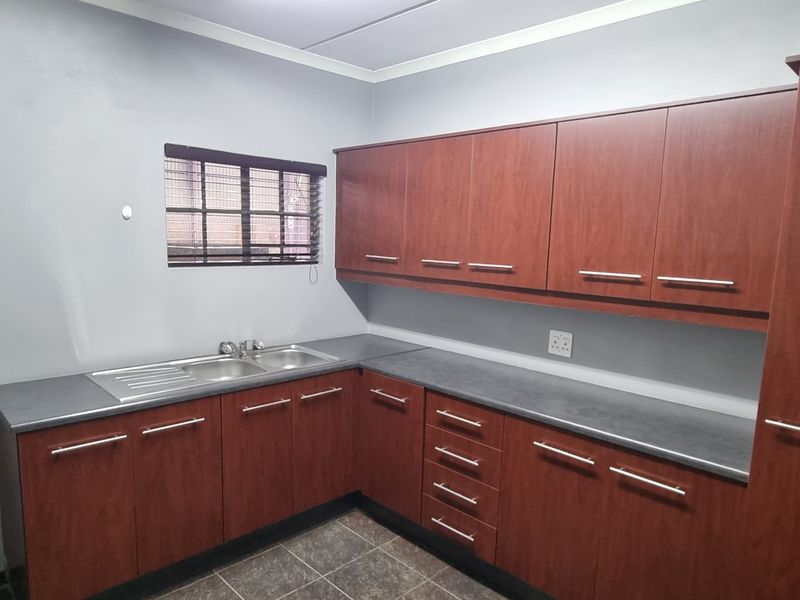 A functional kitchen area featuring wood-look laminate cabinetry, dark countertops, a stainless steel double sink, and tiled flooring.