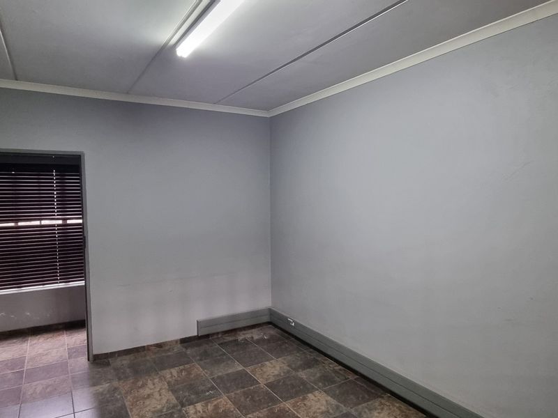 An empty office space featuring tiled flooring, neutral grey walls, and a fluorescent light fixture, suitable for a professional workspace.