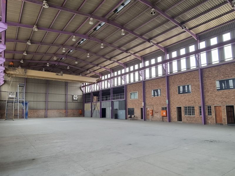 Spacious industrial warehouse featuring high ceilings, exposed steel structural elements, overhead crane, and durable concrete flooring, suitable for manufacturing or logistics operations.
