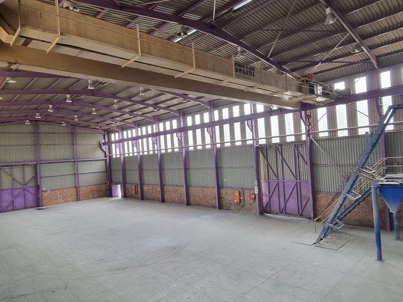 Spacious industrial warehouse featuring a high-clearance steel portal frame, overhead crane system, concrete flooring, and integrated industrial hopper with access stairs.
