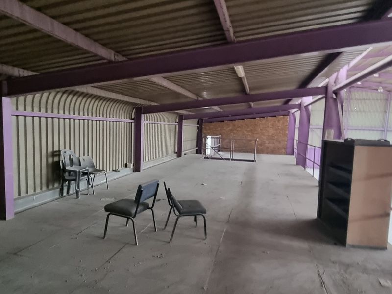 An open-plan industrial mezzanine level featuring exposed steel structural beams, corrugated metal wall cladding, and a metal safety railing.